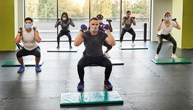 masked gym-goers participate in a group exercise class